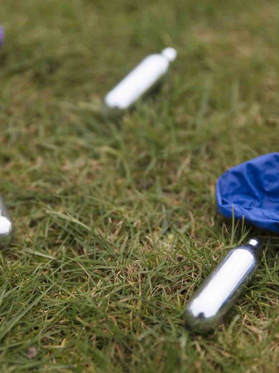 discarded canisters of nitrous oxide and balloons on grass