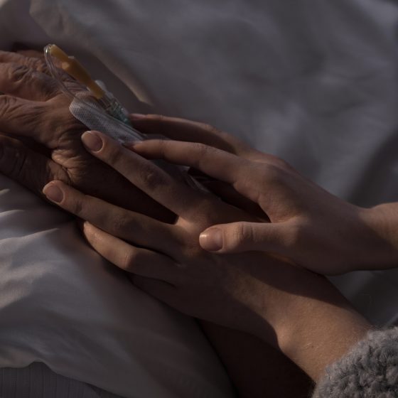 young hand holding hand of elderly cancer patient in care